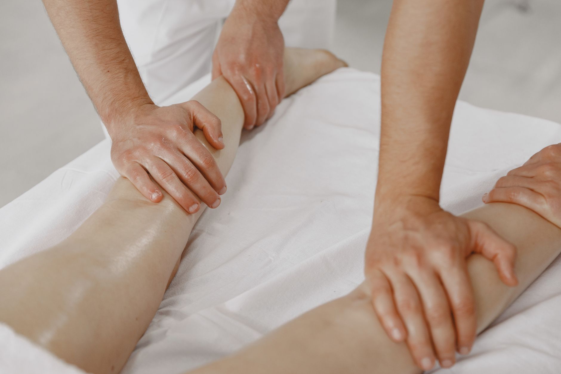 A massage therapist's hands applying light pressure along a client's calf on a treatment table