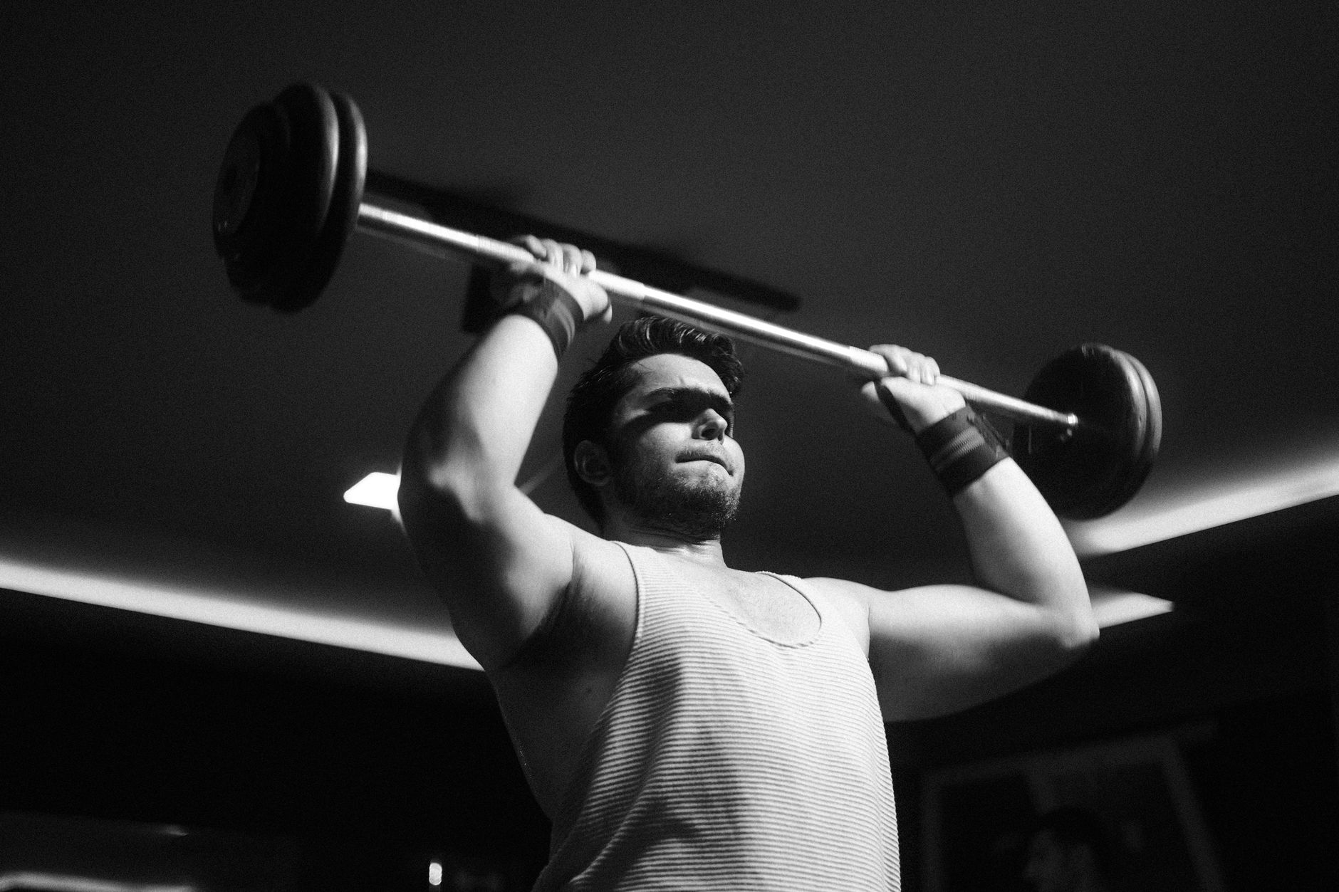 Photo en noir et blanc d'un homme qui pousse une barre au-dessus de la tête dans un gymnase