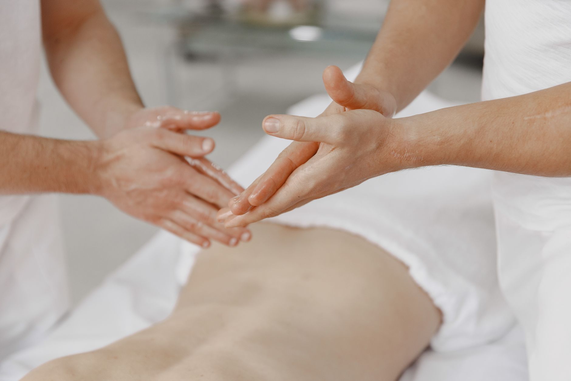 Les mains d'un massothérapeute faisant pénétrer l'huile dans le dos d'un client sur une table de traitement