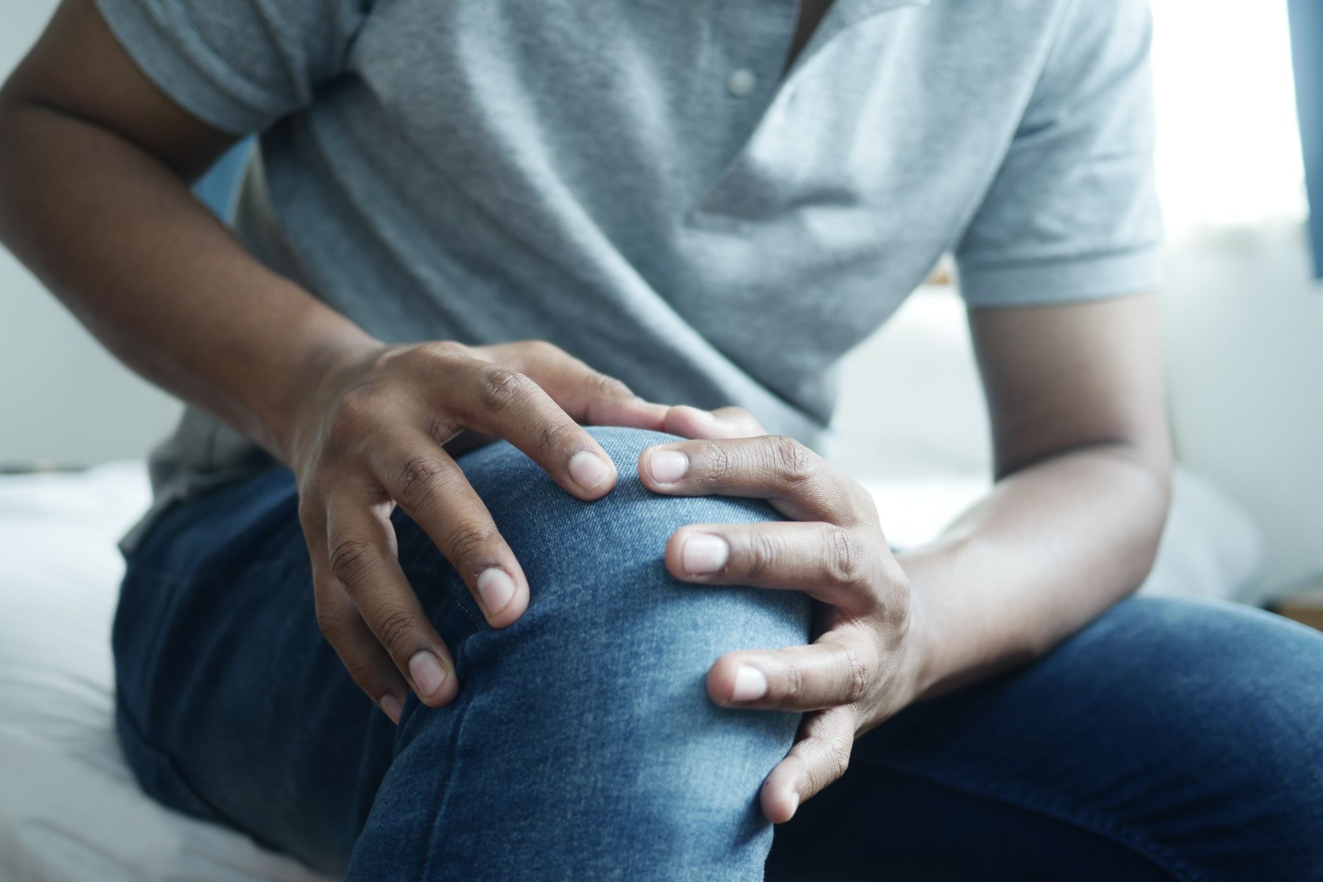 Un homme assis sur un lit tenant son genou à deux mains